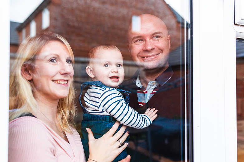 Smiling family looking through window with baby